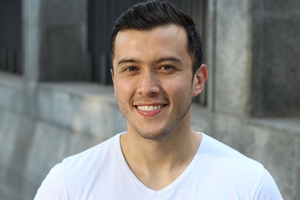 Hombre de 30 años aproximadamente sonriendo, tiene el cabello de color negro y ojos castaños. Usa una playera de color blanco