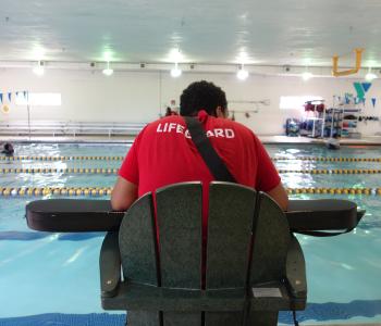 ymca lifeguard sits at stand while on duty keeping water safe