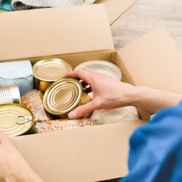photo of person fill cardboard box with nonperishable foods and canned goods 
